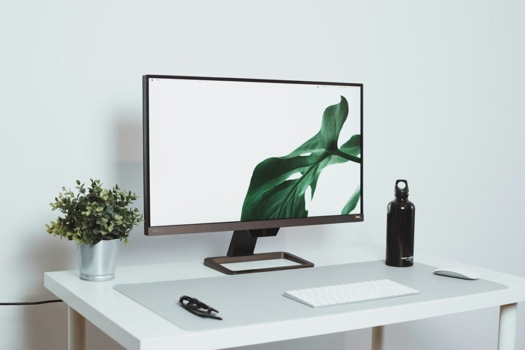Minimal white desk with a monitor, plant, and wireless keyboard